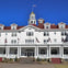A large white building with a red roof, featuring a central cupola and multiple American flags, under a clear blue sky.