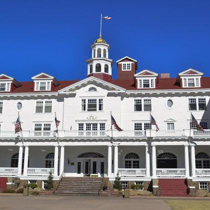 A large white building with a red roof, featuring a central cupola and multiple American flags, under a clear blue sky.