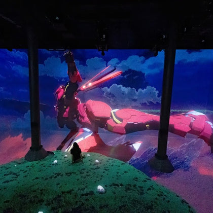 Two people stand in an exhibit surrounded by large screens displaying rock concert scenes. Text reads "Rolling Stone presents AMPLIFIED: The Immersive Rock Experience."