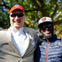 Two men wearing Washington baseball caps and sunglasses smiling outdoors under trees.
