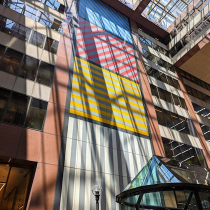 An atrium with a large colorful wall mural featuring geometric patterns and a glass pyramid structure on the ground level.