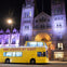 A yellow double-decker bus with "See London by Night" text, parked in front of an illuminated historic building at night.