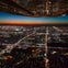 Aerial view of a city at dusk, with illuminated streets and buildings, seen from an airplane window.