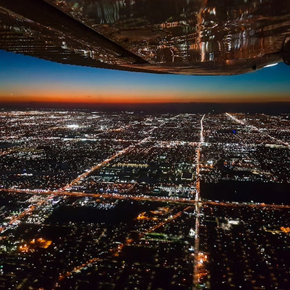 Aerial view of a city at dusk, with illuminated streets and buildings, seen from an airplane window.