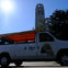 A white van with "The Lombard Leap" branding is parked near trees, with a tall tower and the sun visible in the background.