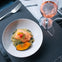 A plate of salmon on risotto, garnished with herbs and squash, with a fork and a glass of rosé wine placed beside it.