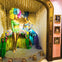 Two mannequins dressed in colorful, feathered showgirl costumes displayed in an ornate window with framed photos on the side.