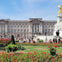 Buckingham Palace with crowds of people and the Victoria Memorial in front, surrounded by vibrant red flowers and greenery.