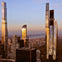 A cityscape at sunset featuring modern skyscrapers with reflective glass facades and a scenic background of buildings and trees.