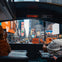 View from inside a vehicle of Times Square, showing bright billboards, busy traffic, and two people at a table.