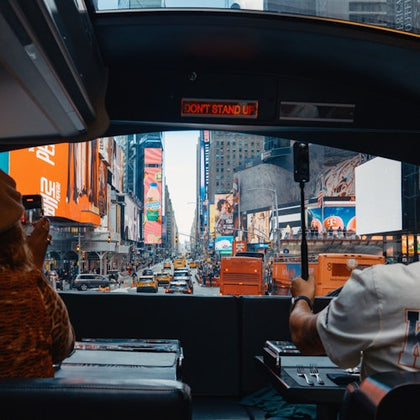 View from inside a vehicle of Times Square, showing bright billboards, busy traffic, and two people at a table.