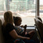 A woman and child sitting on a ferry, with the child looking at a phone and a cityscape visible through the window.