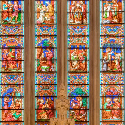 Colorful stained glass windows in a cathedral, depicting various religious scenes and figures, with intricate designs.