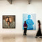 A gallery wall displaying two large paintings; one shows two women, the other a man. A person observes them closely.