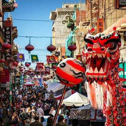 A bustling street festival in Chinatown with a colorful dragon puppet and red lanterns hanging overhead.
