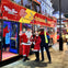 Three people, including one dressed as Santa, stand in front of a red London sightseeing bus at night.