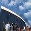 Large ship named "TITANIC" with people on deck and on the dock below, pointing and waving. Blue sky with scattered clouds in the background.