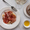 A plate with assorted cured meats, walnuts, and cheese, a loaf of bread, a glass of wine, and olive oil on a marble table.