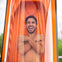 A man smiling inside a transparent orange capsule, crossing his arms, with a blurred outdoor background.