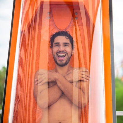 A man smiling inside a transparent orange capsule, crossing his arms, with a blurred outdoor background.