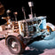 A lunar rover on a dusty surface under bright lighting, showcasing its intricate design and wheels, with a dark background.