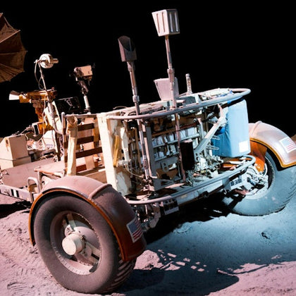 A lunar rover on a dusty surface under bright lighting, showcasing its intricate design and wheels, with a dark background.