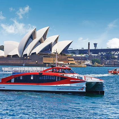 A red and white ferry labeled 'Captain Cook Cruises' on water near the Sydney Opera House and Sydney Harbour Bridge.