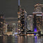 A nighttime cityscape with illuminated skyscrapers reflected on a body of water, featuring a lit-up InterContinental hotel.