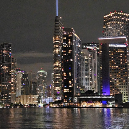 A nighttime cityscape with illuminated skyscrapers reflected on a body of water, featuring a lit-up InterContinental hotel.