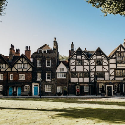 Several connected, historic houses with various architectural styles and blue or white doors, set against a lawn and blue sky.
