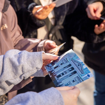 People holding printed photos and documents, one showing a building with columns and a triangular pediment.