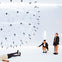 A large transparent sphere with black details is suspended in a bright room. Three people interact with the scene.