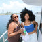 Two women smiling on a boat with a city skyline and water in the background.