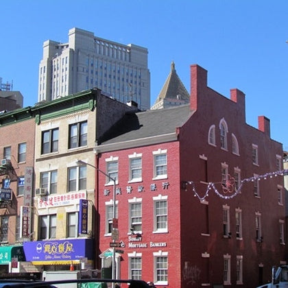 City street with colorful buildings, including a red brick structure and storefronts, under a clear blue sky.