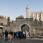 A group of tourists gathered near the entrance of a historic stone castle under a clear blue sky.