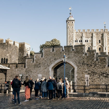 A group of tourists gathered near the entrance of a historic stone castle under a clear blue sky.