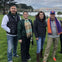 Five people standing on a grassy area with the Golden Gate Bridge and water in the background on a cloudy day.
