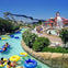 People float in a pool on inflatable tubes near a building with nautical decor and palm trees under a blue sky.