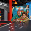 An adult and child happily race colorful LEGO cars on a track in a brightly lit, playful workshop setting.
