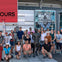 A group of people poses around a statue in an urban setting. Behind them, signs for Vancouver Whitecaps FC are visible.