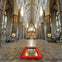 Gothic cathedral interior with vaulted ceilings, grand columns, ornate stained glass, and a decorated plaque on the floor.