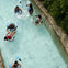 People floating on inflatable tubes in a lazy river surrounded by vegetation.