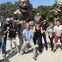 A group of people posing enthusiastically in front of large bronze statues in a park on a sunny day.