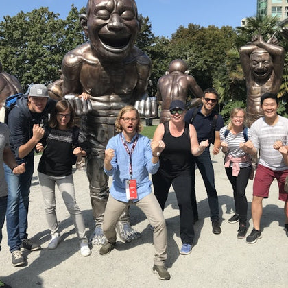 A group of people posing enthusiastically in front of large bronze statues in a park on a sunny day.