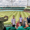 A group of people posing for a photo in a stadium with green seating and a grass field under a cloudy sky.