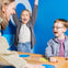 Two children playing a game with a smiling adult, celebrating joyfully, against a bright blue wall background.