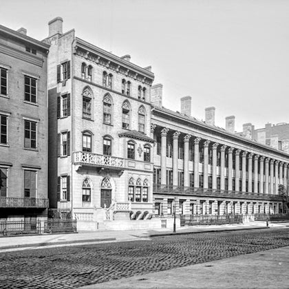 A historic row of buildings with ornate architectural details, including arched windows and a colonnade, along a cobblestone street.