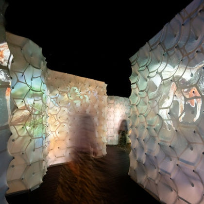 A hallway with illuminated, patterned walls, showing soft projections. Figures are blurred as they walk through.