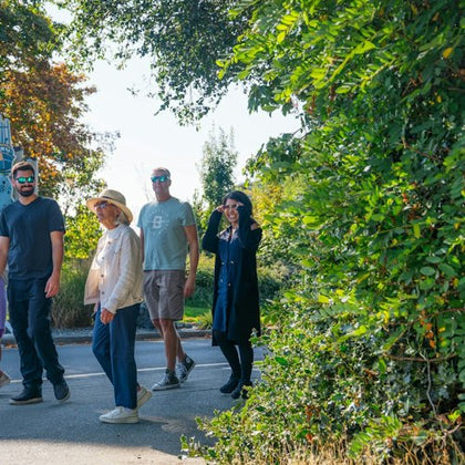 A group of four people walking along a path near trees and greenery on a sunny day.