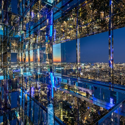 A mirrored room reflecting a cityscape at night with illuminated buildings and a blue sky transitioning to sunset colors.